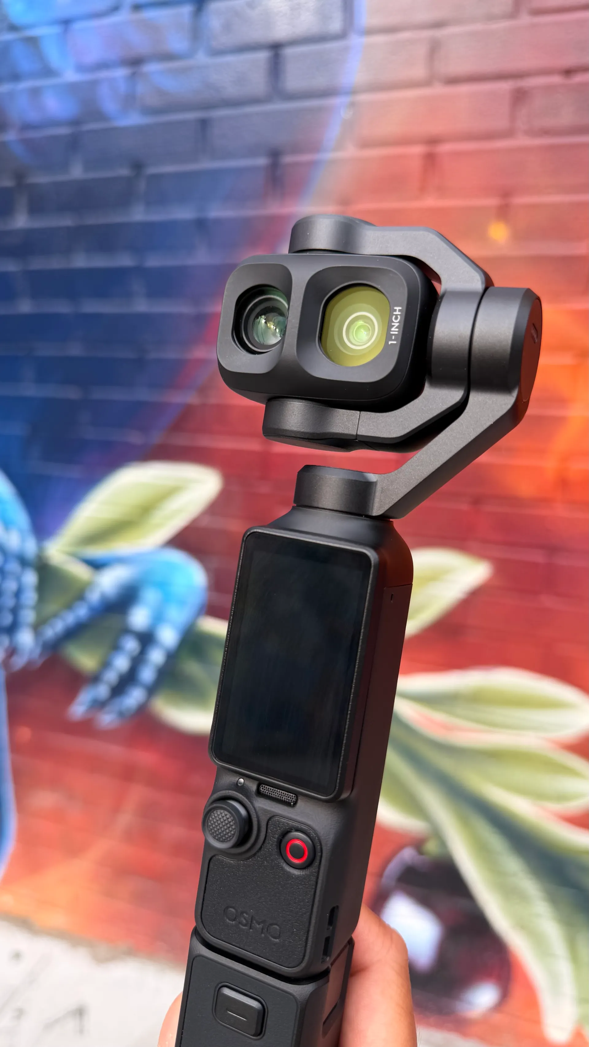 Photo of the DJI Pocket 4P in front of multi-colored graffiti on a brick wall.